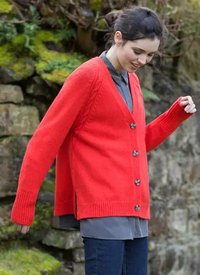 brunette woman in grassy, rocky area wearing bright red cardigan with grey collared shirt underneath